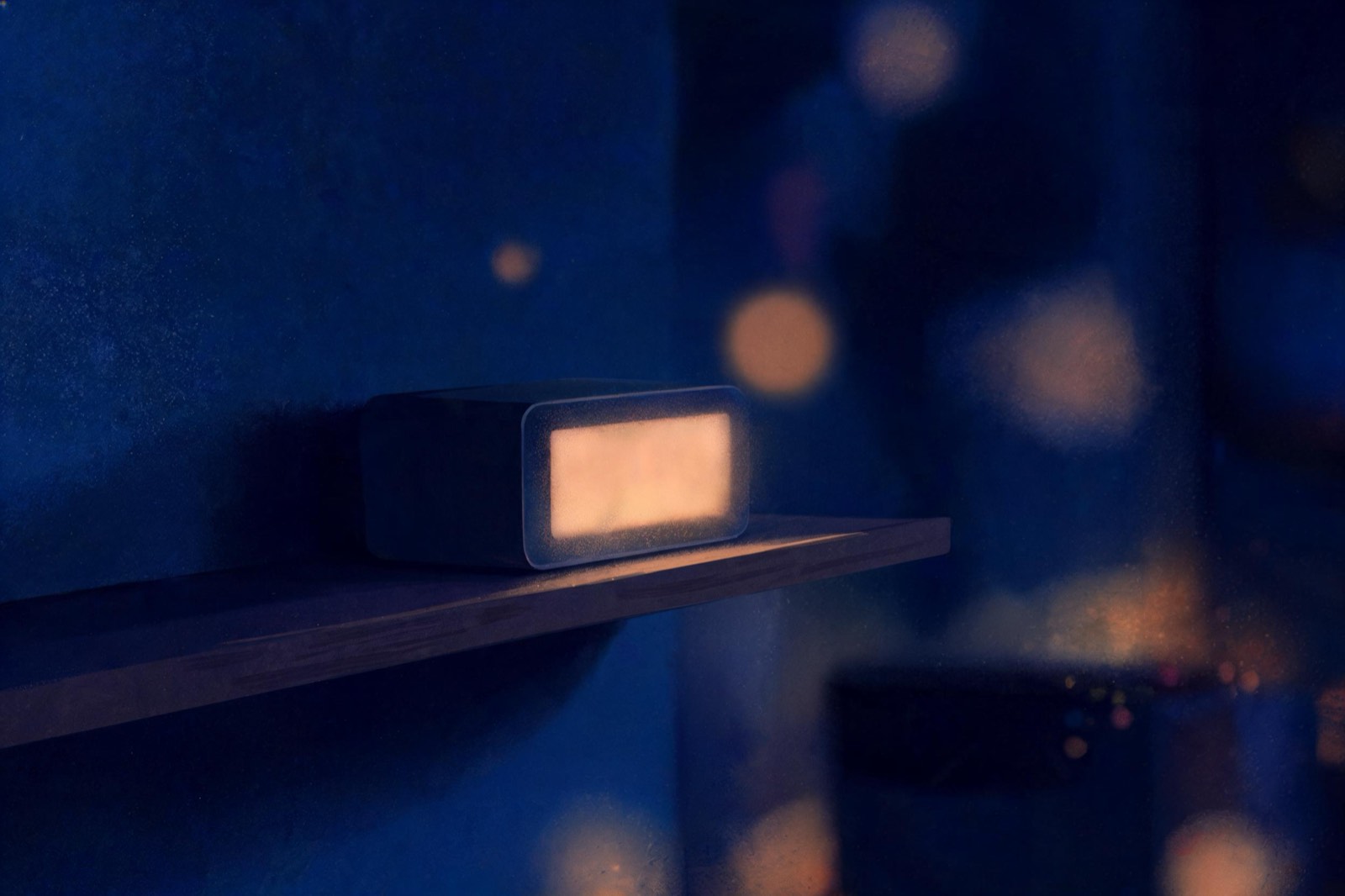 Eine Digitaluhr leuchtet schwach in einem dunklen Zimmer, die Anzeige ist unscharf.